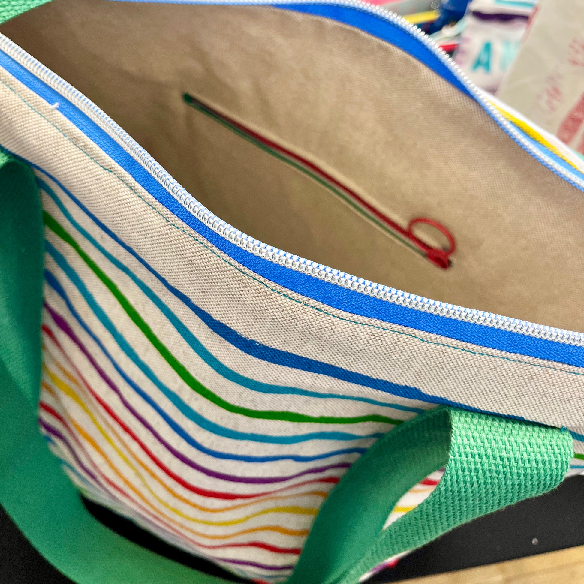 close up of the top zip of a brightly coloured stripey shoulder bag - inside the bag you can see it's lined and has an additional zipped pocket